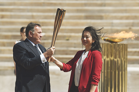◎ 三月十九日,日本代表團成員井本直步子(右)從希臘奧委會主席斯皮羅斯.卡普拉洛斯手中接過東京奧運會聖火火炬。(新華社)