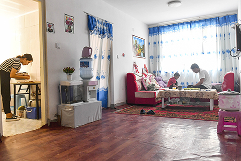 ◎ 7月20日,在縣城家中,古麗斯坦·艾山(左)在廚房做午飯,阿拉帕提·牙森在客廳陪兒子玩遊戲。