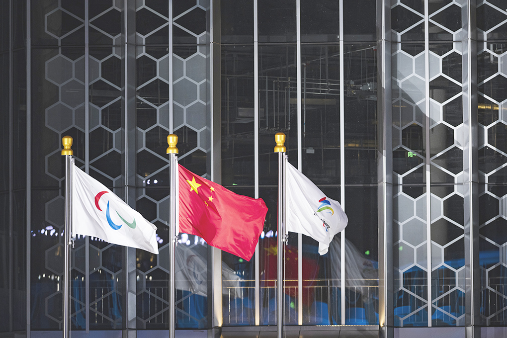 ◎ 三月四日晚間,北京二0二二年冬殘奧會張家口賽區頒獎廣場上,中國國旗、國際殘奧委會會旗(左)和北京冬殘奧會會徽旗幟迎風飄揚。當天,北京二0二二年冬殘奧會開幕。(中新社記者 侯宇 攝)