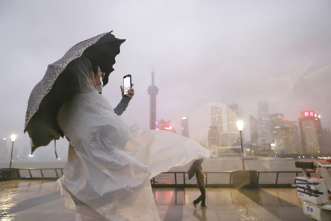 ◎ 九月四日,遊客冒雨在上海外灘濱江步道上拍照。當日下午六時上海中心氣象台更新颱風藍色預警信號為台風黃色預警信號。上海市綠化市容局九月三日發佈了便民提示,受「軒嵐諾」影響,九月四日晚間上海市暫停開放景觀照明。(中新社記者 殷立勤 攝)