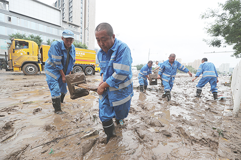 ◎ 八月一日,北京市門頭溝區,北京環衛集團的工人在馮石環路上開展清淤作業。圖為工人從淤泥中搬出隔離護欄,便於大型機械開展作業。(中新社記者 賈天勇 攝)