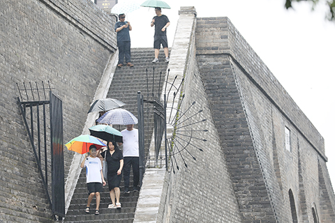 ◎ 八月七日,陝西西安,遊客在雨中步行下城牆。當日,陝西省氣象台繼續發佈暴雨橙色預警信號,關中多地市迎大範圍降雨天氣。(中新社)