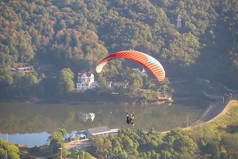 ◎ 十月十八日,滑翔傘定點世界杯總決賽在湖北省荊門市東寶區聖境山生態旅遊區開幕,來自十九個國家和地區的四十八名頂尖運動員齊聚荊門東寶,角逐年度總冠軍。圖為參賽選手滑翔在山水之間。(中新社記者 張暢 攝)