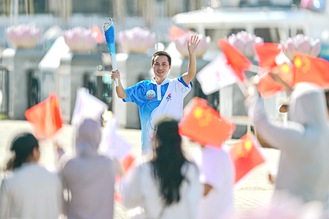 ◎十一月十七日,第十二屆全國少數民族傳統體育運動會火炬實地傳遞活動在海南三亞舉行,一百零七棒來自各行各業的火炬手通過「海陸空」接力方式完成火炬傳遞。圖為第一百零五棒火炬手張保會向現場民眾揮手。(中新社記者駱雲飛 攝)