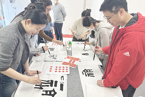 ◎ 馬年將至,位於香港西營盤的中遠青年公寓內,長桌排開,紅紙鋪就,書法老師正指導學生落筆、懸腕。公寓住了逾百戶香港大學的學生,這天特意舉辦寫揮春活動。(香港中通社記者 徐嘉儀 攝)