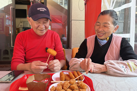 ◎ 三月十一日,台胞劉韋麟(左)與妻子吳微微一邊品嚐自製的台灣小吃一邊聊天。(中新社記者 岳依桐 攝)